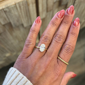 Hand wearing an oval lab grown diamond ring in 14K yellow gold